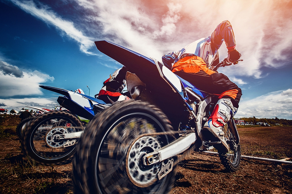 Papier peint photo - Gros plan sur des motos de motocross qui partent en course sur un circuit en plein air, sous un ciel bleu avec des nuages