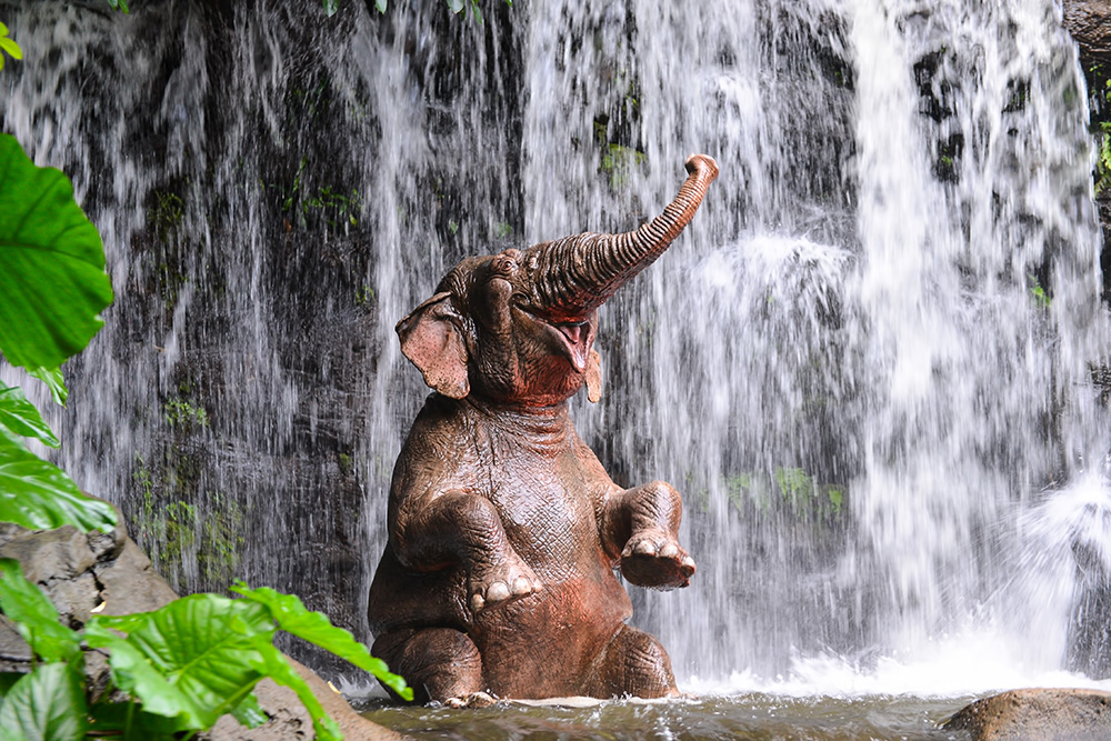 Papier peint photo - Un éléphant prend une douche sous une cascade, entouré de plantes tropicales