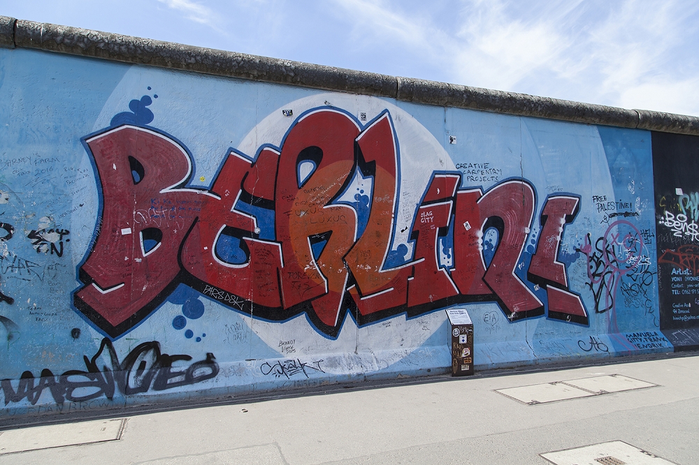 Papier peint photo - graffiti 'Berlin' sur le mur de Berlin, entouré d'un mur et d'un ciel bleus