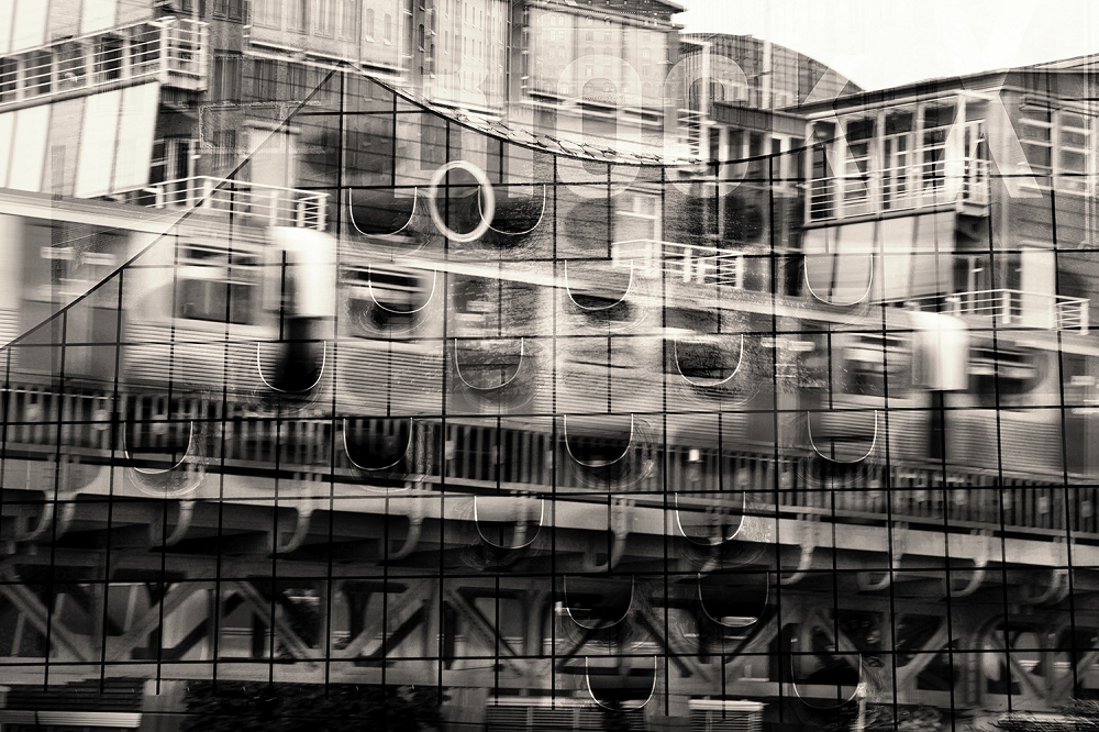 Papier peint - photographie en noir et blanc d'une scène urbaine avec un reflet montrant des bâtiments et un train qui passe