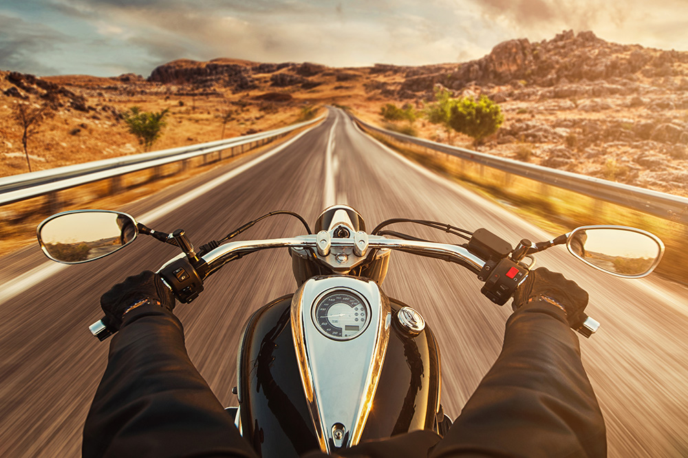 Papier peint photo - vue d'un motard sur une longue route sinueuse à travers un paysage sec et vallonné au coucher du soleil