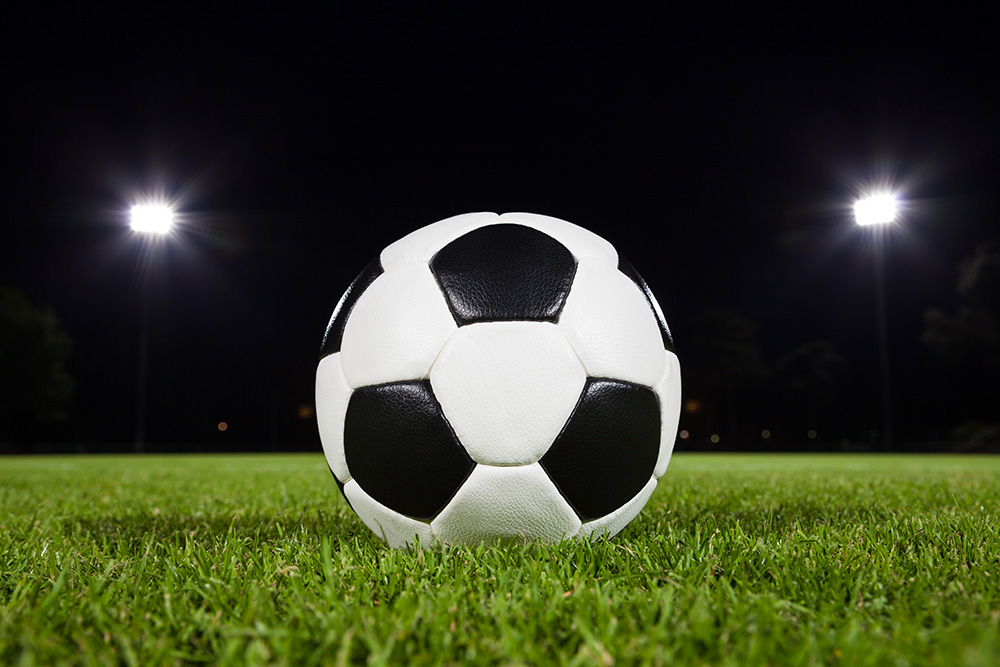 Papier peint photo - Football noir et blanc sur gazon vert, entouré de projecteurs qui illuminent un terrain de nuit