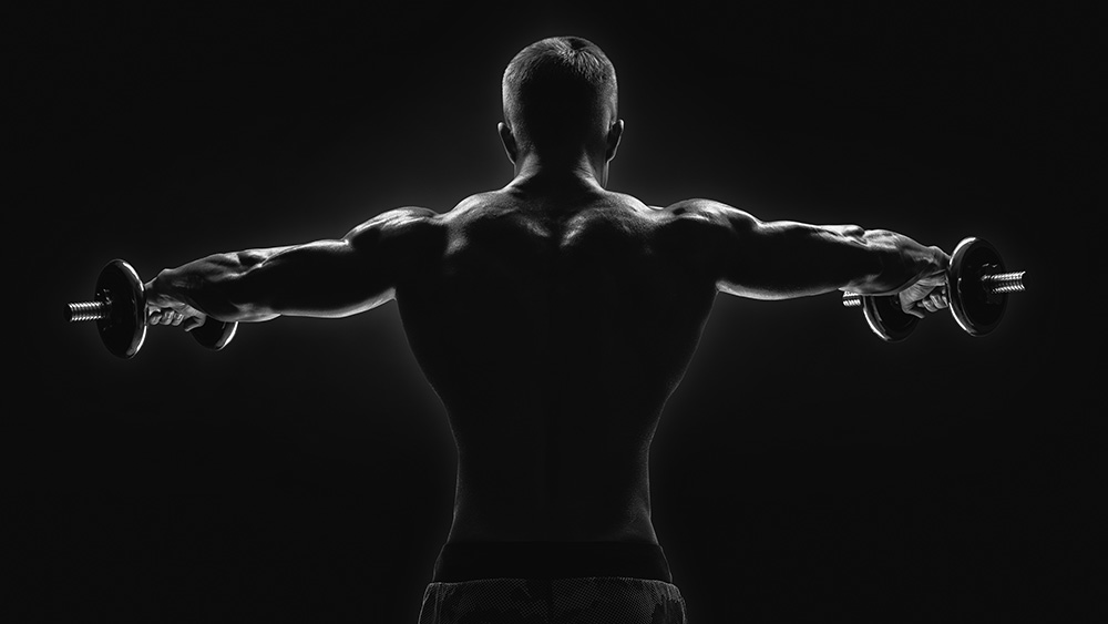 Papier peint photo - vue de dos d'un homme musclé soulevant des haltères dans une prise de vue en noir et blanc très évocatrice