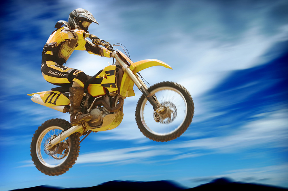 Papier peint photo - Un motocrossman sur une moto jaune saute en l'air devant un ciel bleu