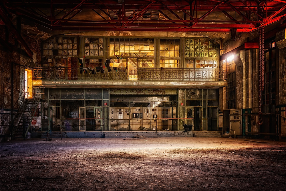 Papier peint photo - Intérieur d'une usine abandonnée, éclairée par une lumière chaude, avec des poutres en acier rouge et un sol poussiéreux
