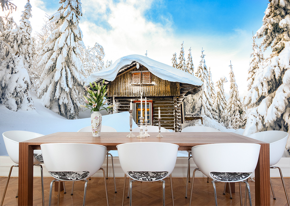 Papier peint photo - Un chalet de montagne en bois rustique entouré d'une forêt dense et enneigée par une claire journée d'hiver.