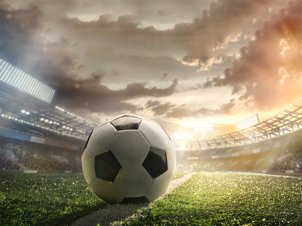 Papier peint photo - Un ballon de football est allongé sur un terrain éclairé dans un stade, alors que le soleil se couche à l'horizon. Scène parfaite pour les fans de football.