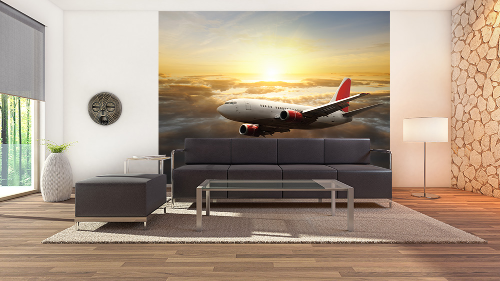 Papier peint photo - Un avion vole au-dessus des nuages au coucher du soleil, décore un mur de salon avec des meubles modernes.