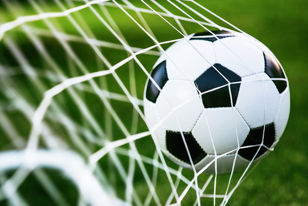 Papier peint photo - Un ballon de foot coincé dans un filet de but sur un terrain vert